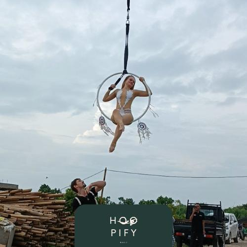 Aerial performer suspended in Hoopify Bali hoop against open sky